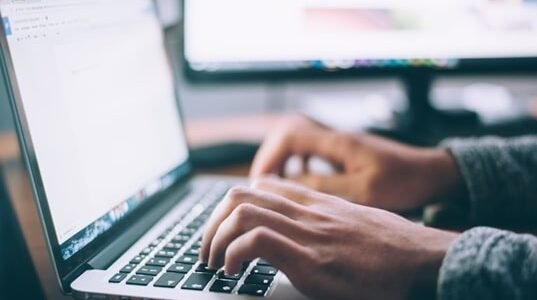 A professional working on their laptop to access information using a self-service knowledge base of their organization.